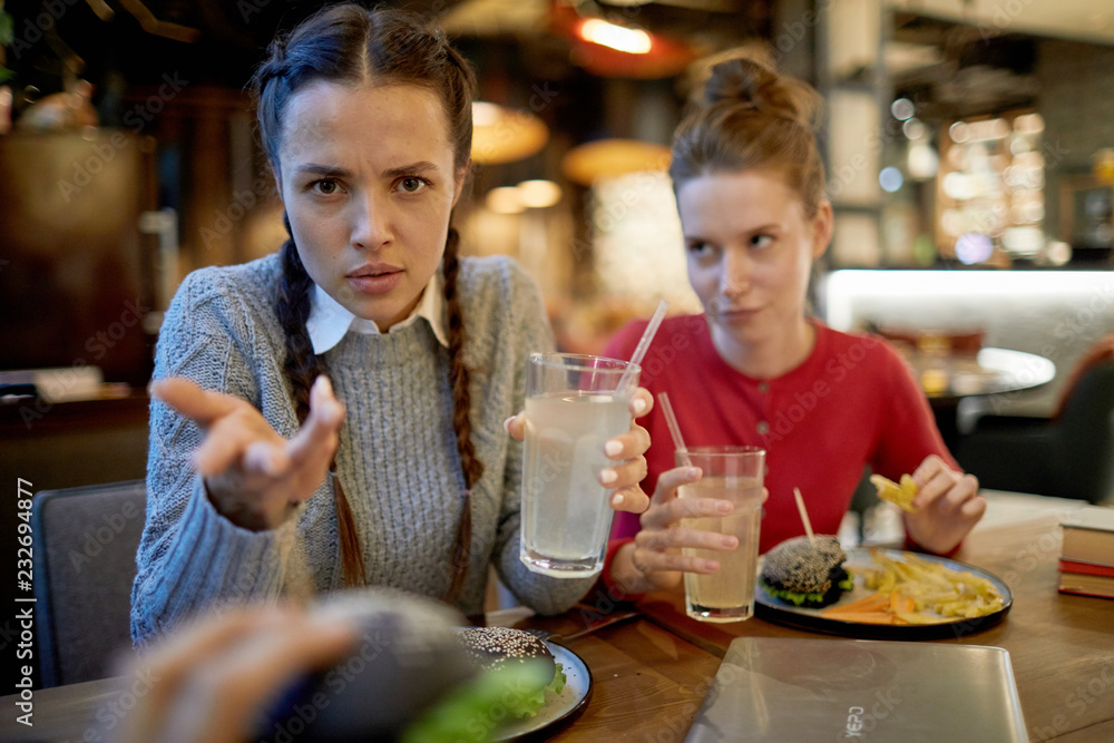 Rude girl in casualwear looking at you with aggressive expression while having lunch with friends