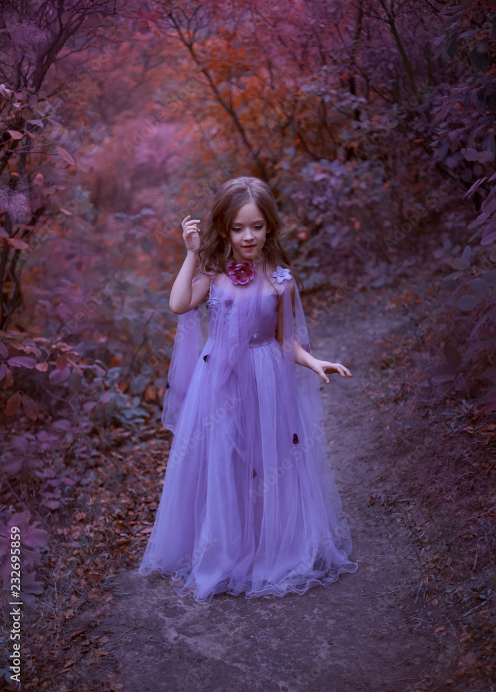 cute girl is standing in the forest in a purple light long dress with flowers, a little princess like in a dream, walks along the path in the maroon garden, straightens her brown hair, looks down
