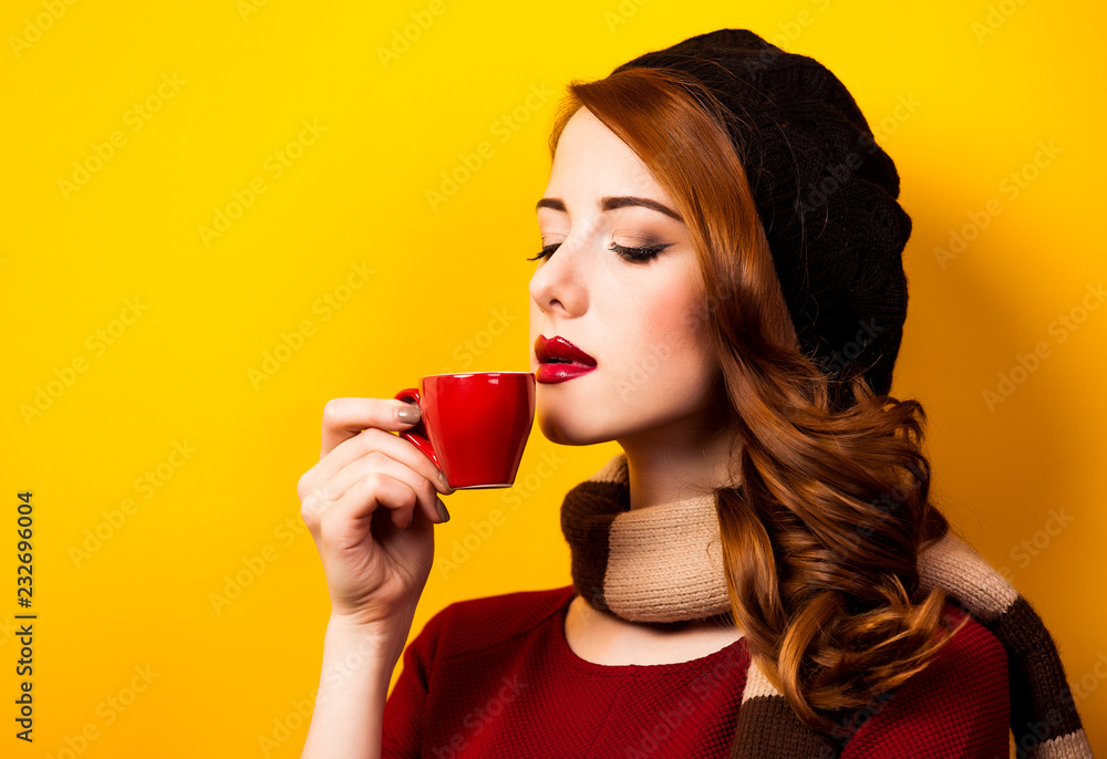 Redhead girl in french beret with red cup of coffee or tea on yellow background. Redhead girl in french beret with red cup of coffee or tea on yellow background.