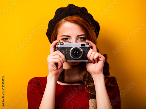 Redhead woman in beret with scarf and vintage camera on yellow background.