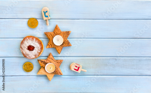 Wooden candlesticks in the shape of star  donut  golden chocolate coins and dreidels on background of blue painted wooden planks with space for text. Jewish holiday Hanukkah. Top view  flat lay