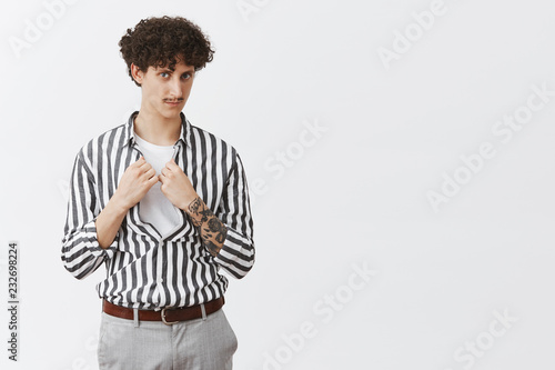 Deal for such smart and determined guy like me. Portrait of self-assured good-looking and stylish creative male with curly hairstyle moustache and tattoos buttoning shirt and smiling at camera