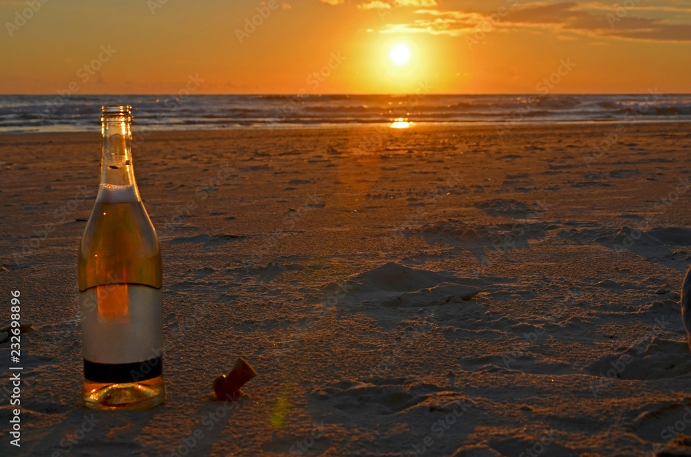 An open bottle of champagne stands with a cork stopper on the sand. Meeting of the sunset on the Mediterranean Sea in Israel. An open bottle of champagne stands with a cork stopper on the sand. Meeting of the sunset on the Mediterranean Sea in Israel.