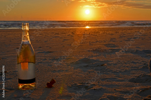 An open bottle of champagne stands with a cork stopper on the sand. Meeting of the sunset on the Mediterranean Sea in Israel.