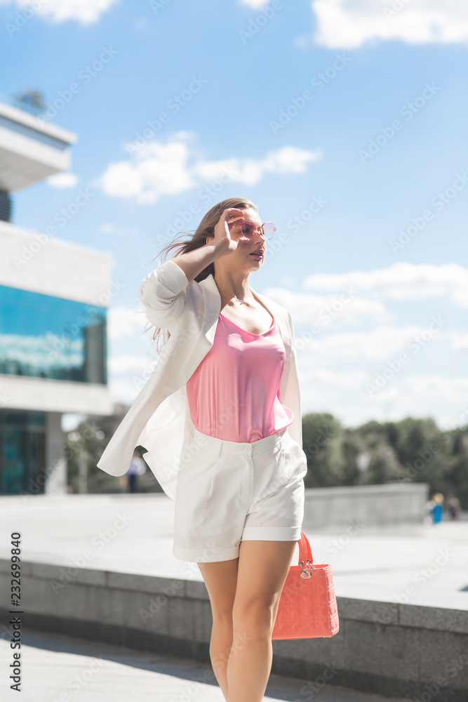 Woman on city background. Business woman on urban landscape wearing white jacket and shorts.