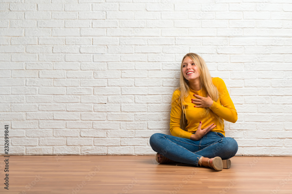 Young girl sitting on the floor smiling a lot while putting hands on chest