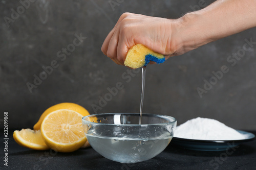 Fototapeta Naklejka Na Ścianę i Meble -  Woman squeezing out sponge over bowl with water and baking soda on dark table