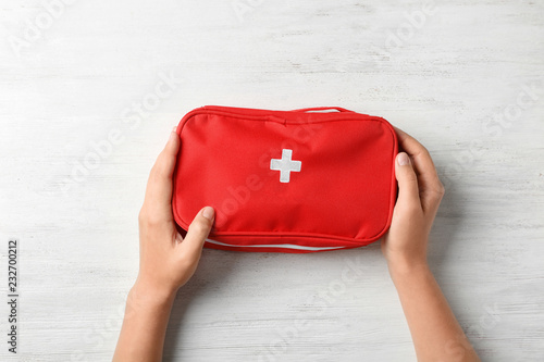Woman holding first aid kit on wooden background, top view