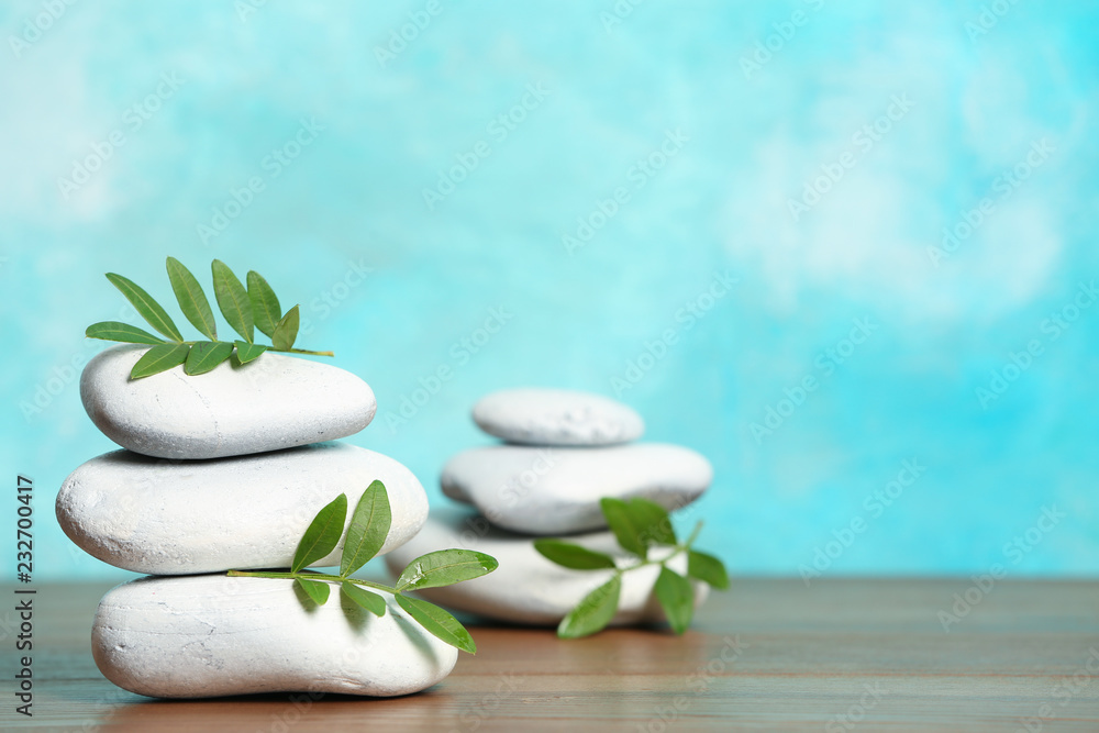 Spa stones and bamboo leaves on table against color background. Space for text Spa stones and bamboo leaves on table against color background. Space for text