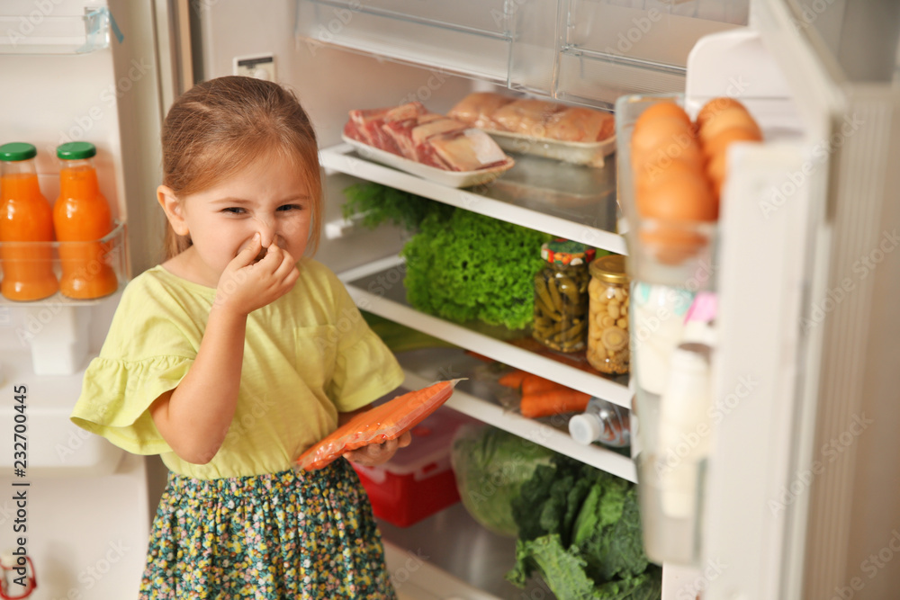 Cute little girl with bad smelling sausages near refrigerator at home Cute little girl with bad smelling sausages near refrigerator at home