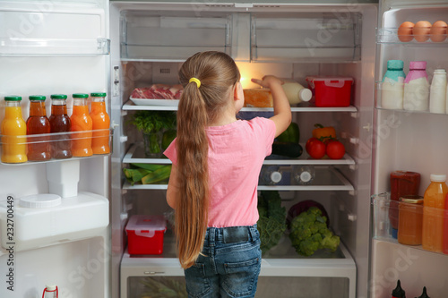 Cute little girl choosing food in refrigerator at home
