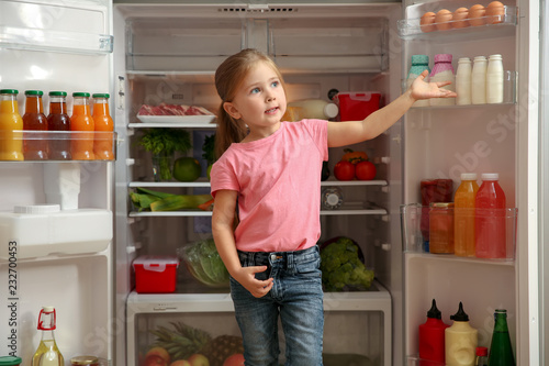 Cute little girl standing near open refrigerator at home
