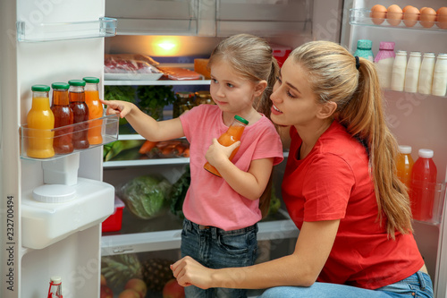 Young mother and daughter choosing juice in refrigerator at home