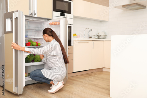 Young woman choosing products from refrigerator in kitchen