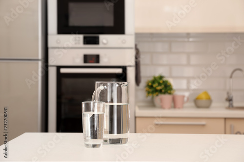 Jug and glass with water on table in kitchen. Space for text