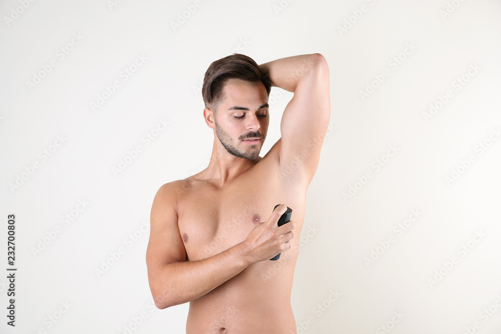 Fototapeta premium Young man using deodorant on white background