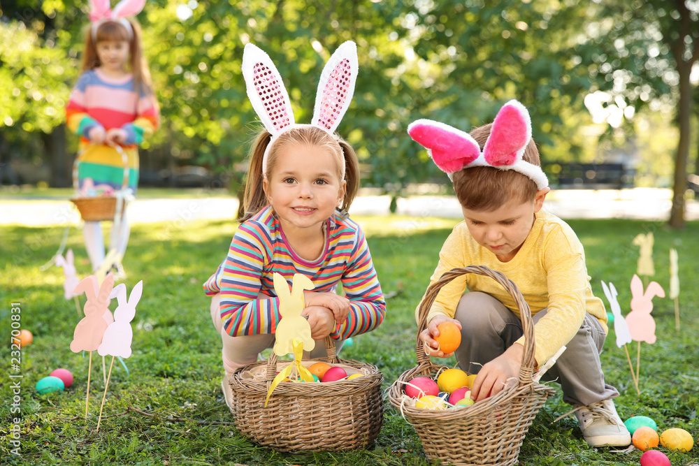 Fototapeta premium Cute little children hunting eggs in park. Easter tradition