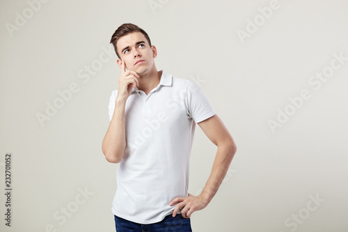 Thoughtful guy dressed in a white t-shirt and jeans is on a white background in the studio