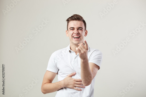 Guy dressed in a white t-shirt and jeans laughs and keeps hand on the belly on a white background in the studio