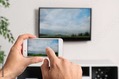 Woman with smartphone connected to TV set in living room