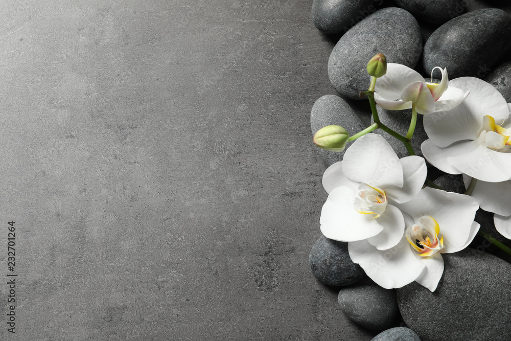 Fototapeta premium Płaska kompozycja świeckich kamieni spa i kwiatów orchidei na szarym tle. Miejsce na tekst