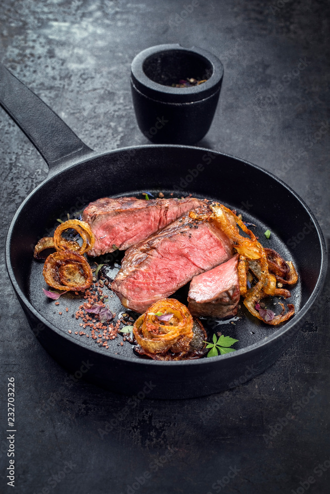 Modern Style classic dry aged sliced roast beef with fried onion rings served as closeup in a minimalistic design cast-iron skillet