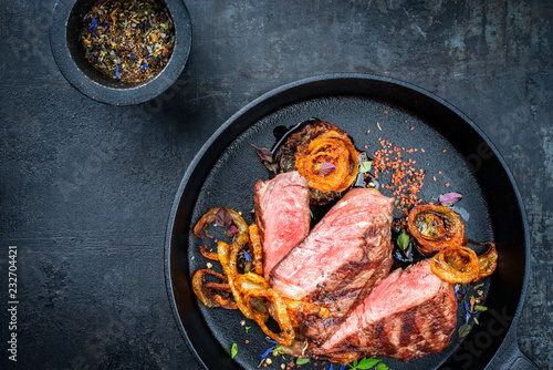 Modern Style classic dry aged sliced roast beef with fried onion rings served as top view in a minimalistic design cast-iron skillet