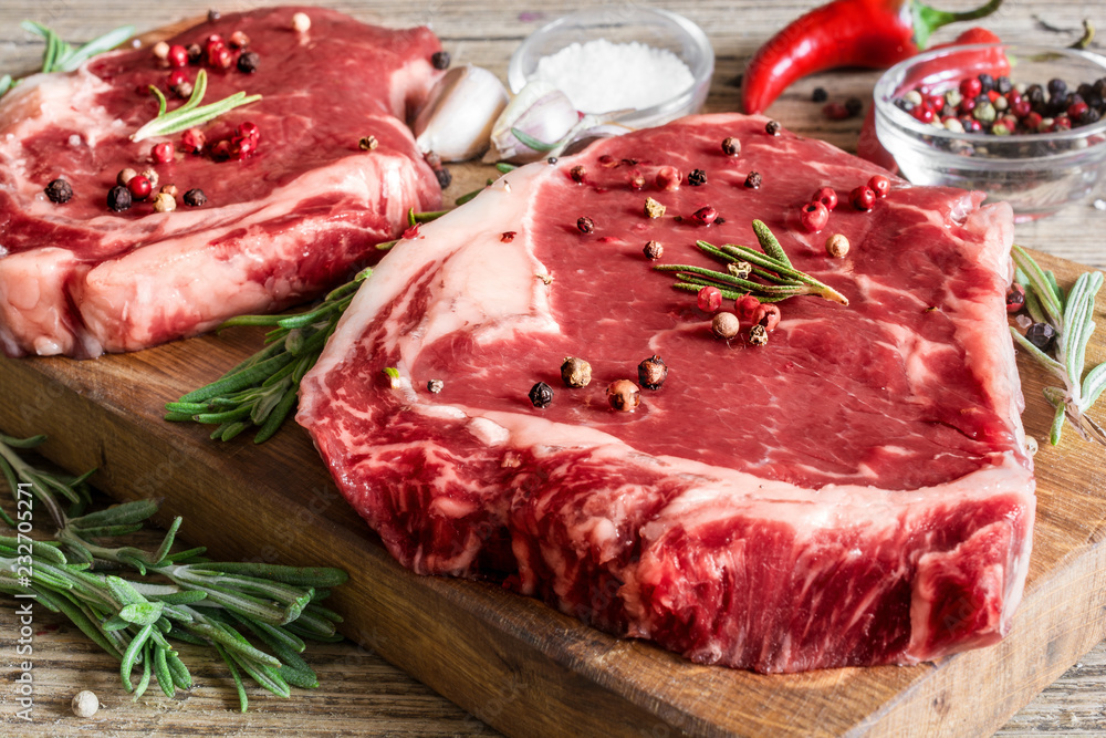 barbecue rib eye steaks with spices, rosemary and chili pepper on wooden cutting board. cooking concept