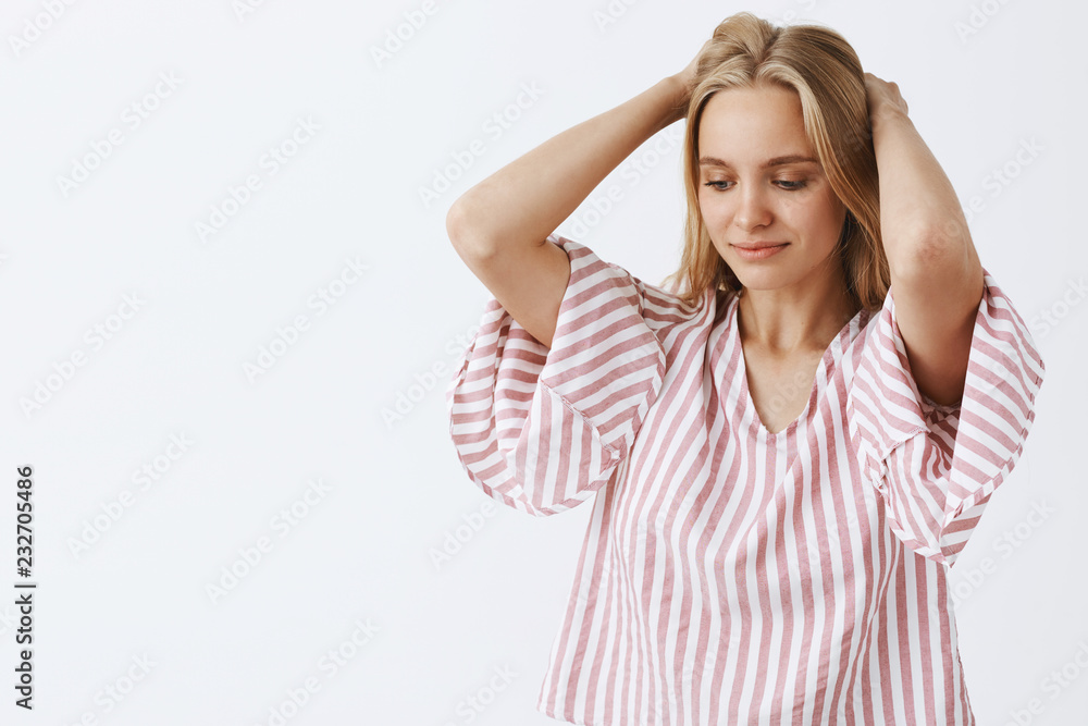 Waist-up shot of dreamy tender and feminine blonde caucasian woman in pink striped blouse holding hands behind head, gazing down with gentle slight smile thinking or imaging something Waist-up shot of dreamy tender and feminine blonde caucasian woman in pink striped blouse holding hands behind head, gazing down with gentle slight smile thinking or imaging something