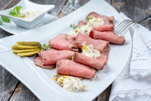 Traditional lunch meat with sliced cold cuts roast beef and remoulade as closeup on a white plate on a wooden table