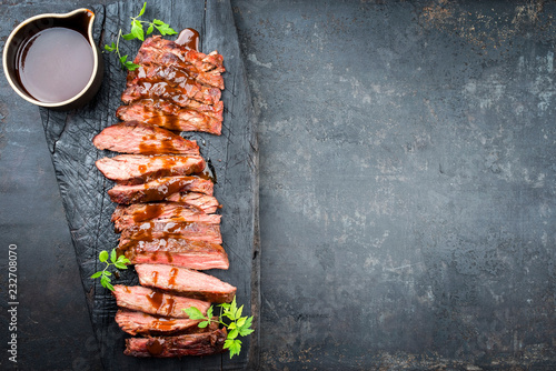 Traditional American barbecue dry aged flank steak sliced with hot sauce and chili as top view on an old carbonized board with copy space right