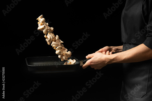 Professional cook. The chef prepares a dish with champignon mushrooms in a saucepan. on a black background. menu, recipe book, healthy food, restaurant business