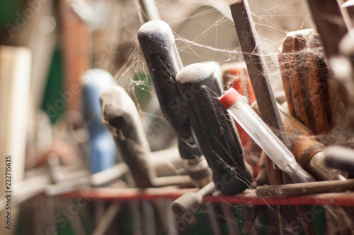 Abandoned tool rack near the barn window. Tools covered in cobwebs. 