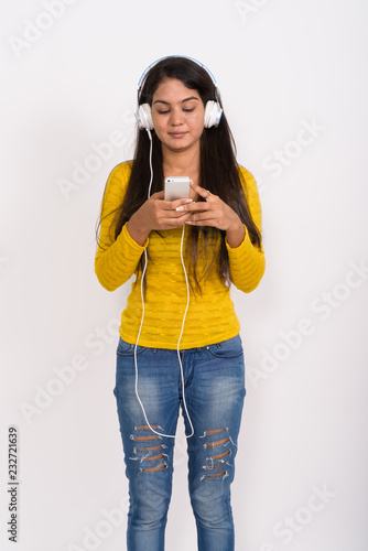 Studio shot of young Indian woman standing while listening to mu
