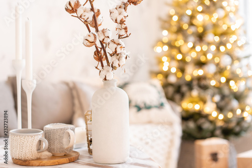vase with cotton branches. Light living room with Christmas tree. Comfortable sofa  high large Windows