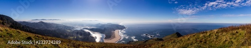 A pano of the Cascade Head overlooking the Salmon River. Looks south toward Lincoln City the river worms its way to the Pacific Ocean on the right. Blue sky and clouds can be seen in the distance.