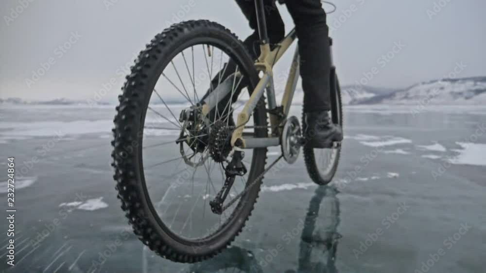 View of tire. Shooting 180fps. Man is riding bicycle on the ice. The cyclist cuts in front of the camera. Pieces of ice fly in us. Ice of the frozen Lake Baikal. The tires on the bicycle are covered View of tire. Shooting 180fps. Man is riding bicycle on the ice. The cyclist cuts in front of the camera. Pieces of ice fly in us. Ice of the frozen Lake Baikal. The tires on the bicycle are covered