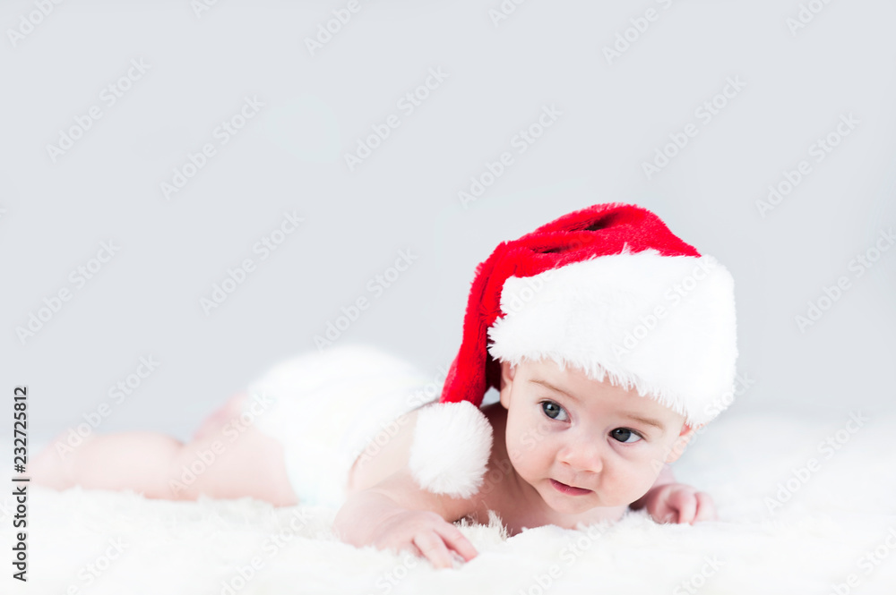 very beautiful bright emotional happy little baby in Santa hat crawling on white plaid very beautiful bright emotional happy little baby in Santa hat crawling on white plaid