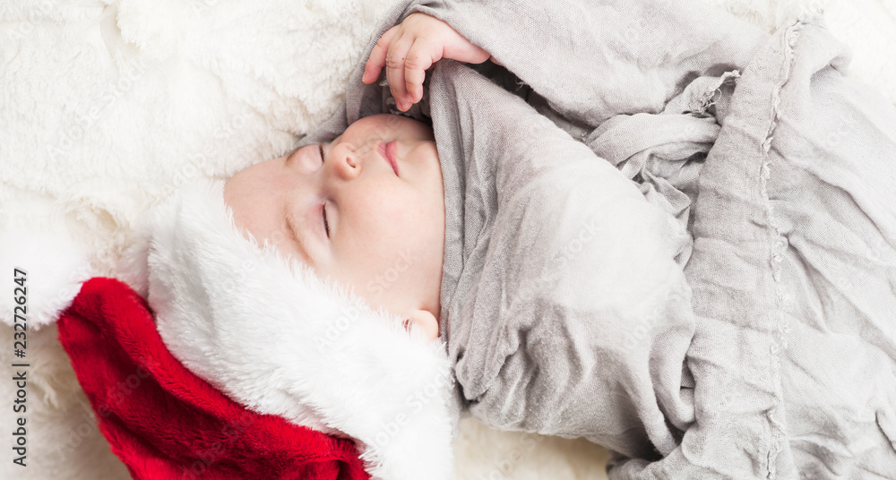 very beautiful bright happy little baby in Santa hat sleeping on white plaid wrapped in grey fabric on black background