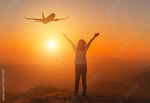 Silhouette back of woman stand raising up two arm celebrate enjoying on high cliff mountain during airplane flying in sunset time, freedom concept 