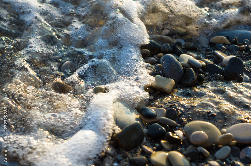 pebble stones on the sea beach, the rolling waves of the sea with foam