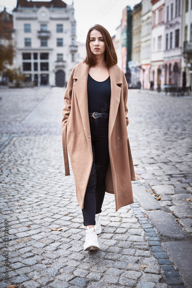 Sensual portrait of a young woman in brown coat. Woman posing outdoors on the street at overcast autumn day