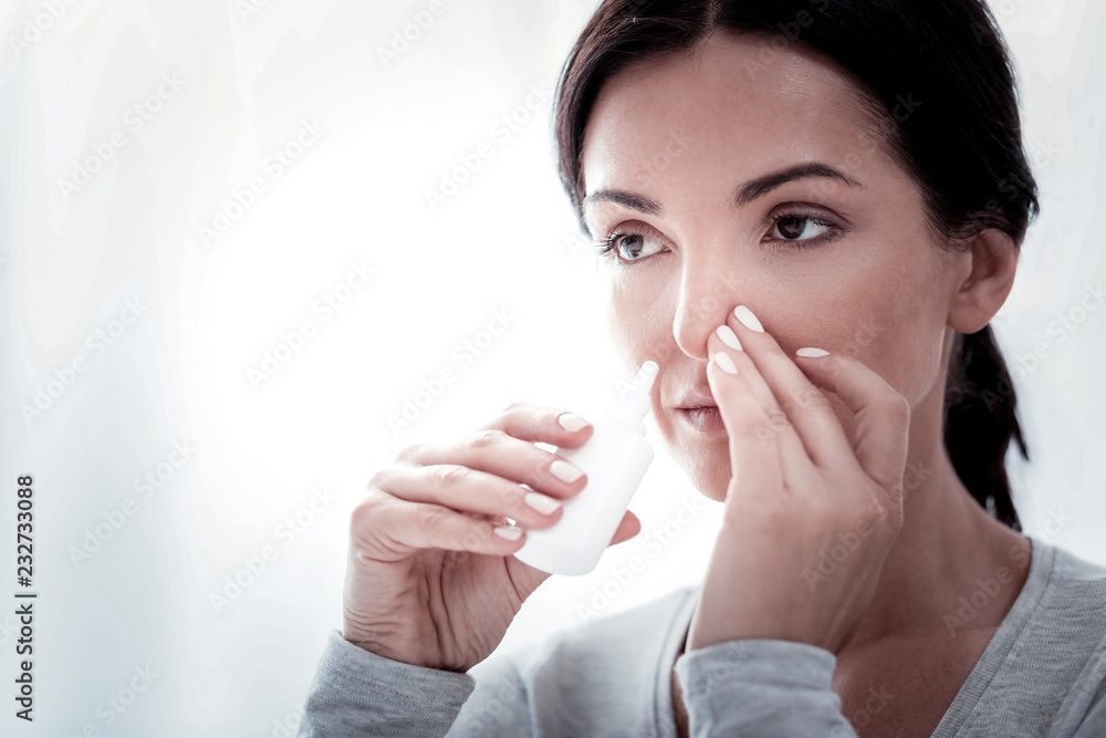 Getting cold again. Portrait of young woman looking away while touching her nose and using nasal drops Getting cold again. Portrait of young woman looking away while touching her nose and using nasal drops