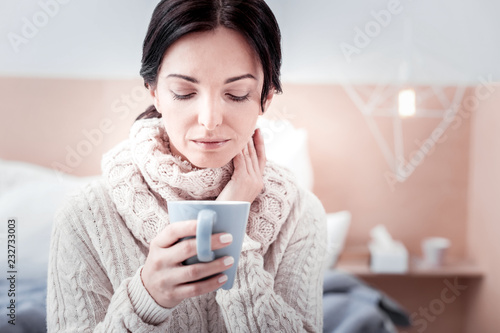 Feeling relaxed. Portrait of young peaceful woman holding a cup of tea while looking at it and expressing quietness