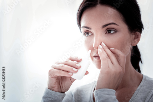 Getting cold again. Portrait of young woman looking away while touching her nose and using nasal drops