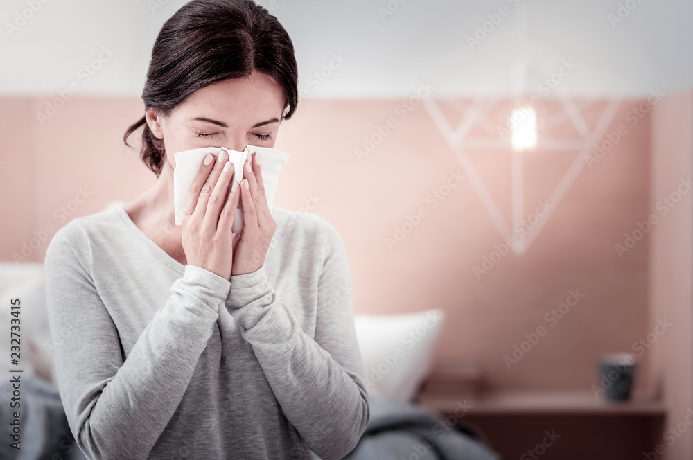 Feeling awful. Close up of young woman using a handkerchief while keeping her eyes closed and blowing her nose - obrazy, fototapety, plakaty 