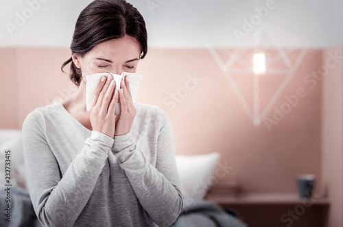 Feeling awful. Close up of young woman using a handkerchief while keeping her eyes closed and blowing her nose