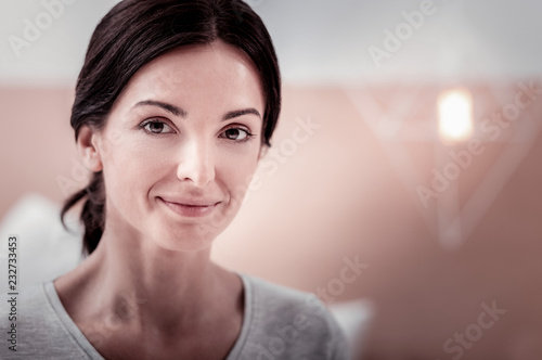 Charming glance. Close up of young good looking woman smiling at you while expressing kindness