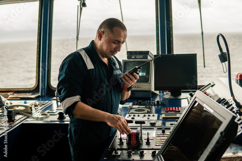 Marine navigational officer is changing speed ship or vessel during navigation watch. He speaks with engine room by walkie-talkie uhf radio photo