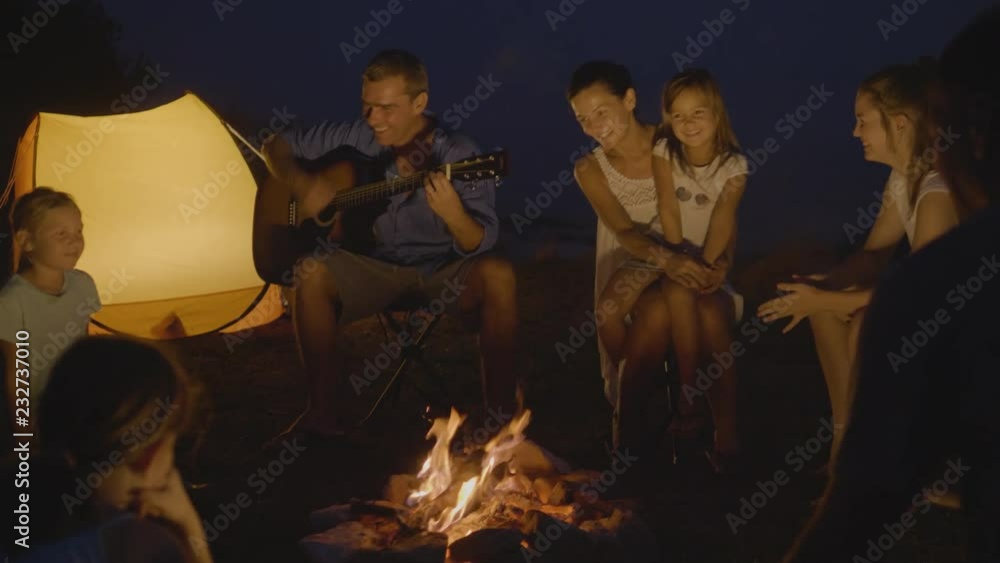 Friends sitting around a campfire, playing the guitar and singing Friends sitting around a campfire, playing the guitar and singing